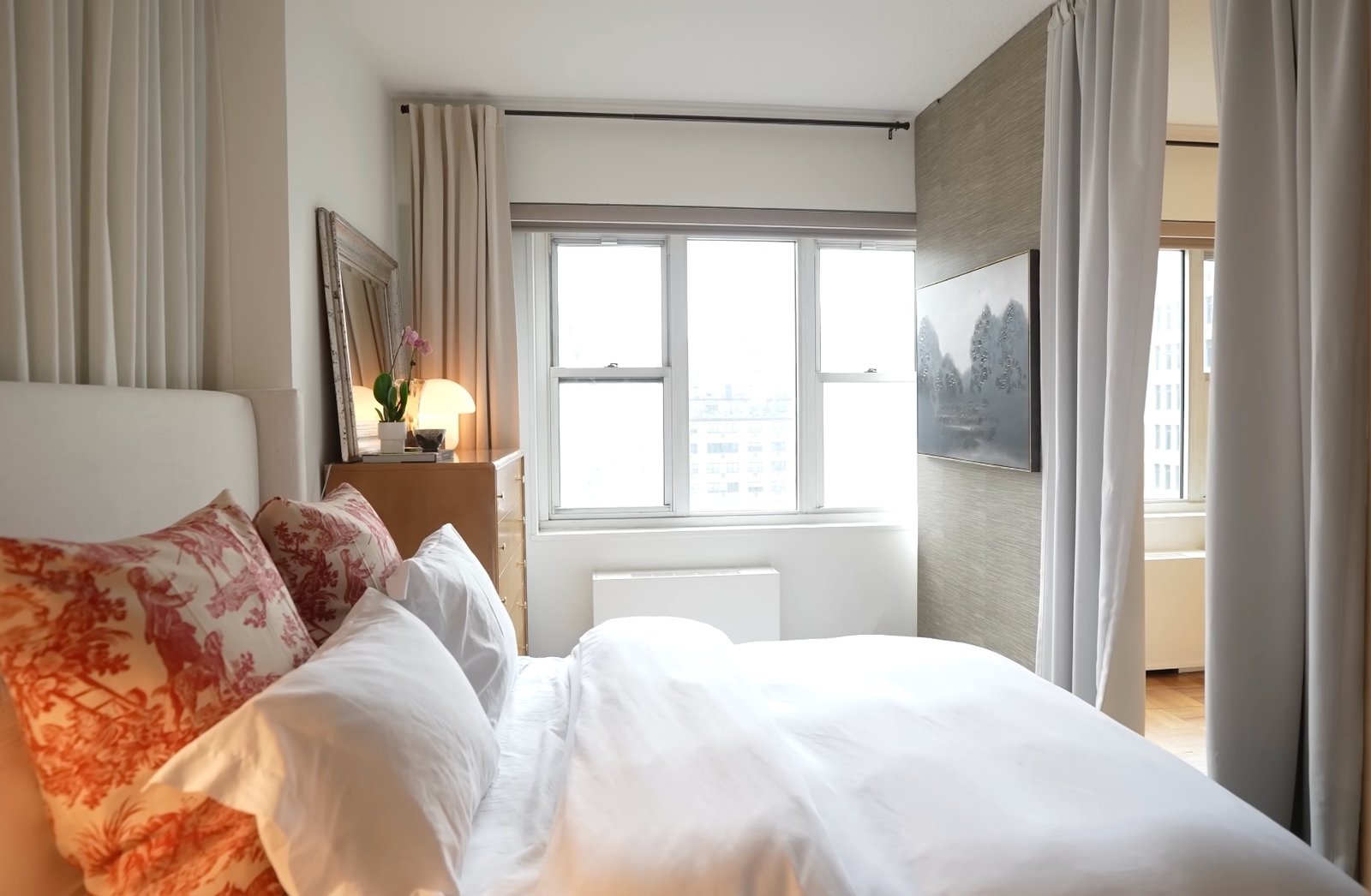 Light-filled bedroom with toile pillows, city views, and grasscloth walls