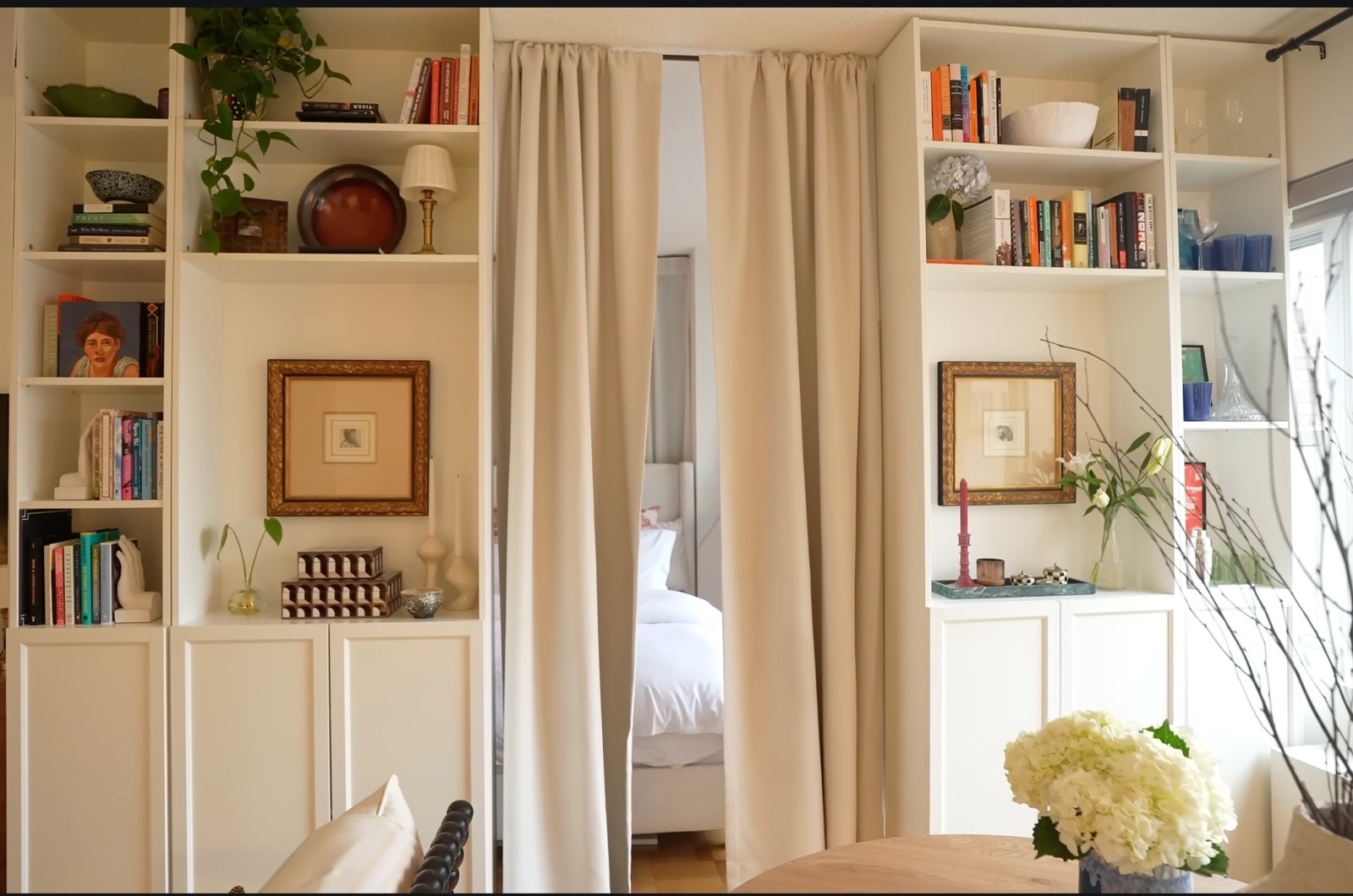 Custom built-in bookshelves flanking draped bedroom entrance with curated art and objects