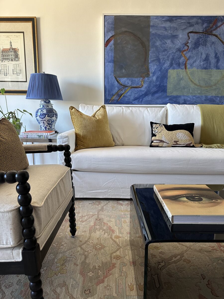 Curated living room with white sofa, blue abstract art, chinoiserie lamp, and bobbin chair